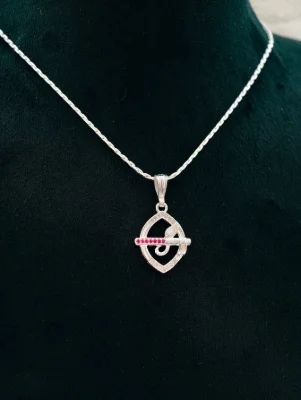 Silver chain with a Krishna flute locket featuring small white stones and red stones.