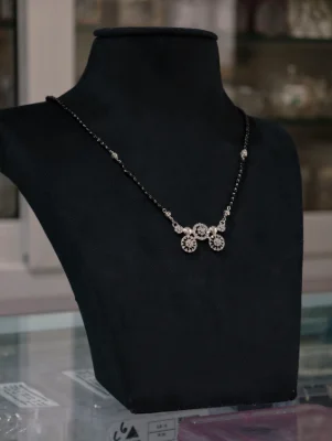 An elegant silver dorla mangalsutra featuring a sparkling stone-studded pendant on a black beaded chain.
