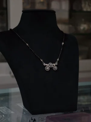 Silver mangalsutra featuring a delicate black bead chain and a sparkling circular patterned pendant.