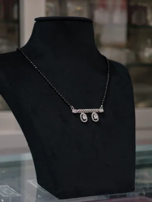 Silver mangalsutra with black beaded chain and a stone studded horizontal bar hanging two oval stone drops.