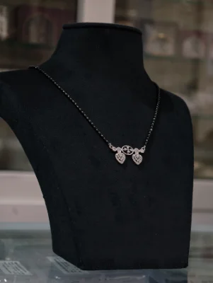 A delicate silver mangalsutra featuring a central heart shaped pendant with small white stones and a black bead chain.