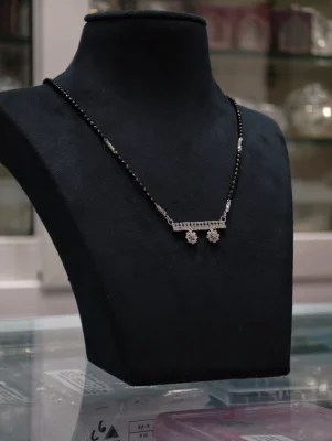 Silver black bead dorla mangalsutra featuring a stone studded horizontal pendant with two dangling floral charms.
