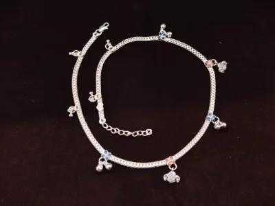 This silver children payal features a chain design adorned with small multi-coloured flower motifs and tiny dangling bells.