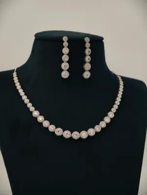 A silver stone necklace set featuring matching drop earrings with sparkling white stones in a round pattern.