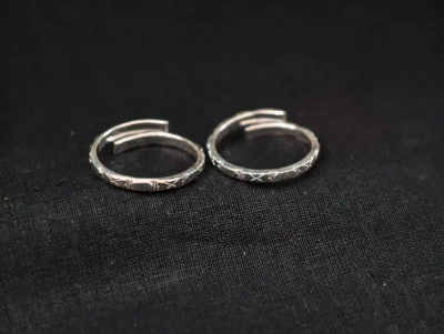 A pair of adjustable silver toe rings featuring a simple band with a subtle engraved cross pattern throughout the surface.