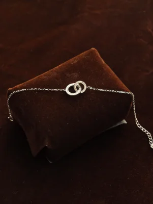 Delicate silver chain bracelet featuring two interlocking rings as a central motif.