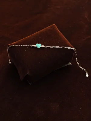 Delicate silver bracelet featuring a turquoise heart charm with wings and a mixed link chain.