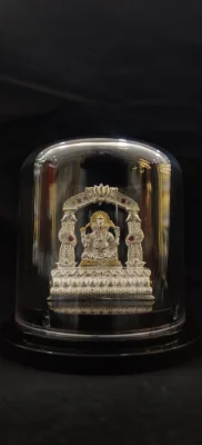 Silver Ganesha idol under a glass dome with ornate arch and red stones.