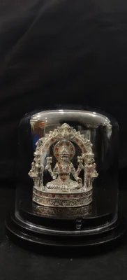 Glossy silver idol featuring a seated deity under an arch with red stones and detailed floral patterns.