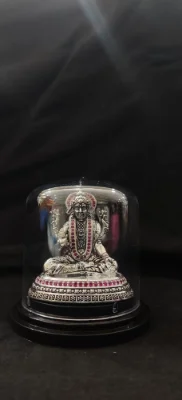 An ornate silver idol of a deity featuring intricate detailing and embedded red stones on a decorative round base.