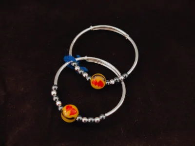Silver kada pair featuring glossy silver beads and a central yellow bead with red heart pattern.