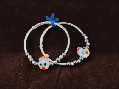 These silver baby kada feature smooth metal bands with small dark beads and a cute snowman charm on each piece.