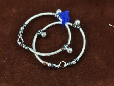 Glossy silver kadli featuring dark faceted beads and small hanging bells.