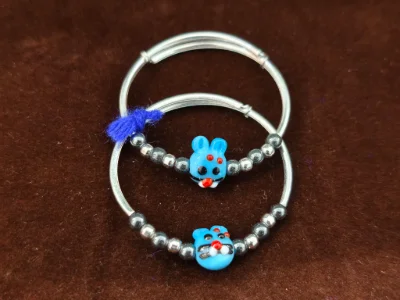 This pair of silver kadli features a cute blue cartoon character bead and small dark metallic beads.