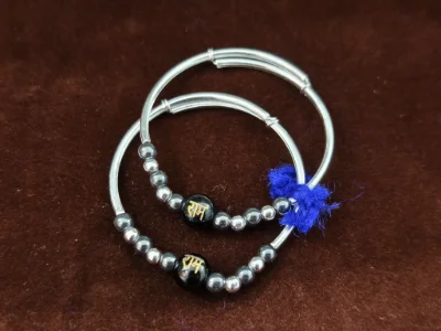 Silver kada pair featuring glossy black beads with Ram inscription and small metallic beads.
