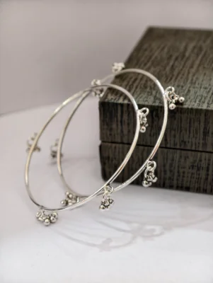 A pair of simple circular silver bangles featuring delicate hanging ghungroo beads at regular intervals with a smooth polished finish.
