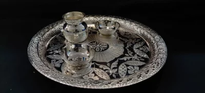 A shiny silver worship thali set featuring engraved floral patterns, a small lota, and two bowls for rituals.