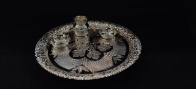 This round silver worship thali features floral engraved patterns with a glossy finish, accompanied by matching small bowls and a pot.