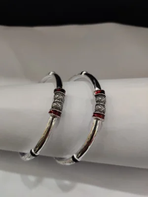 Silver kada pair featuring intricate textured patterns and red enamel accents on a polished surface.