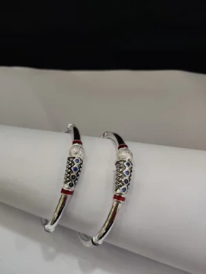 Silver kada featuring textured pattern, red enamel accents, and blue stones.