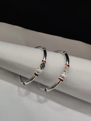 A pair of shiny silver bangles featuring a hollow round design with decorative red and green enamel accents and textured beads.