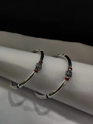 Glossy silver bangles feature a central floral motif with red and blue accents and textured ends.