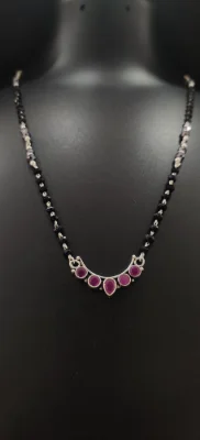 Silver mangalsutra featuring a crescent locket with five pink stones and a chain of black beads.