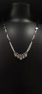 Oxidised silver mangalsutra featuring a curved locket with white stones, black beads, and double chains.