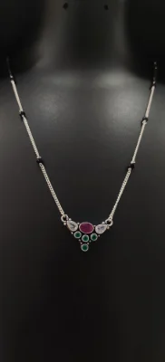 Oxidised silver mangalsutra with black beaded chain and central pendant featuring red, green and white stones.
