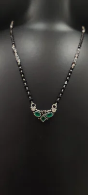 Oxidised silver mangalsutra featuring a curved locket with green and white stones on a black beaded chain.