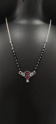 This oxidised silver mangalsutra features a central locket with red and white stones on a delicate black beaded chain.