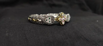 Oxidised silver bracelet featuring floral motifs, intricate patterns, and sparkling white, green, and red stones with gold polish touches.