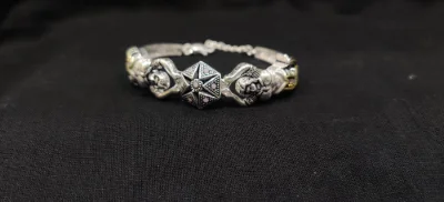This silver bracelet features a central geometric motif with small pink stones and figural elements in an oxidised finish.