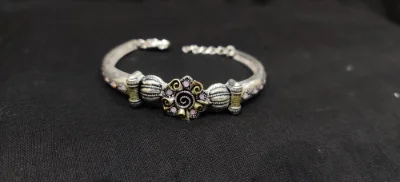 Silver oxidised bracelet featuring a floral centrepiece with pink stones and ornate metallic patterns.