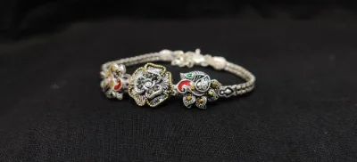 Oxidised silver bracelet featuring floral and peacock motifs with red, green, and black details on a patterned chain.