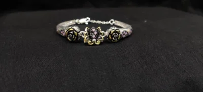 Oxidised silver bracelet featuring black flower motifs, pink enamelling, and a central lotus design with chain extension.