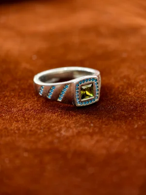 Silver gents ring featuring a square green central stone surrounded by blue stones and diagonal rows on the band.