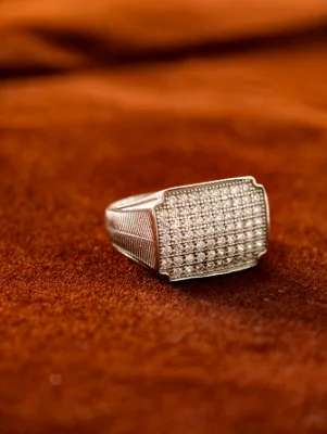 A wide silver male ring featuring a rectangular top paved with small white stones and grooved patterns on the band.