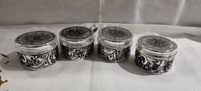 Round silver soap dish with floral engraved lids and ornate black and silver side patterns.