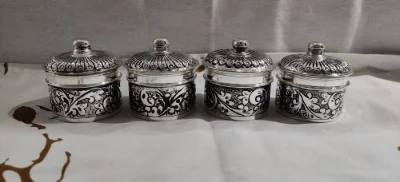 Four round silver soap dishes feature intricate floral patterns and ridged lids with round knobs.