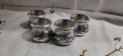 These round silver containers feature a polished finish with intricate floral engravings and a small stone on the lid.