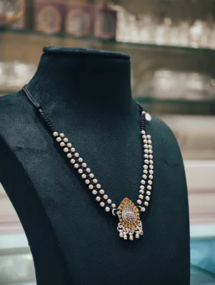 This oxidised silver mangalsutra features a dual black beaded chain with a pear shaped pendant accented with small colourful stones.