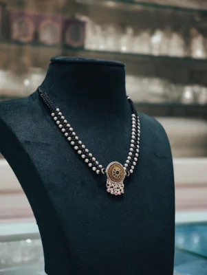 This oxidised silver mangalsutra features a round pendant with green and pink accents strung on two black beaded silver chains.