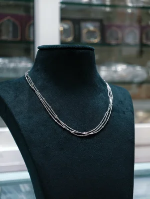 A shiny silver beaded chain features three delicate layers with small spaced beads along the metal strands.