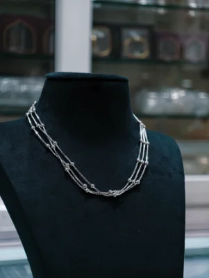 A shiny silver beaded chain features three layered strands with small round beads.
