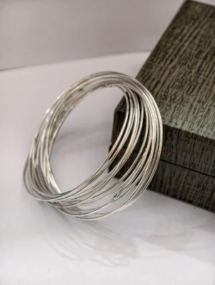These round silver bangles feature a plain interlocking multi wire design with a shiny finish.