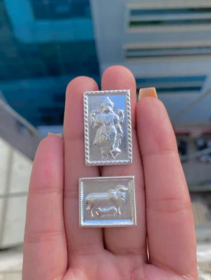 Two rectangular silver yantra pieces feature embossed religious figures with a shiny finish and detailed border patterns.
