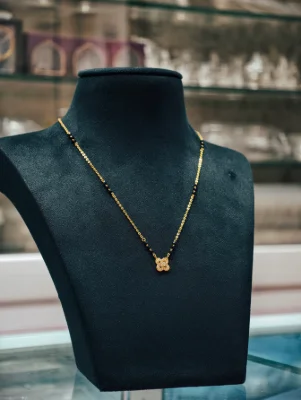 A silver mangalsutra featuring a floral pendant with tiny white stones and a black and gold beaded chain.