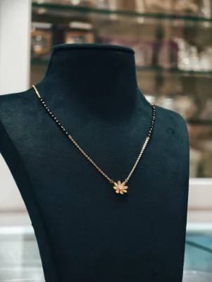 A silver mangalsutra featuring a delicate flower pendant and black beaded chain.