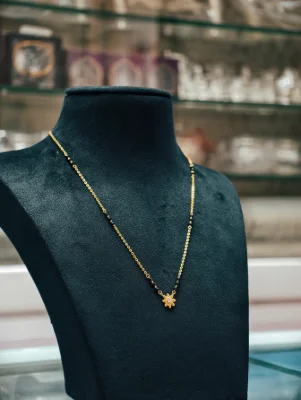Delicate silver mangalsutra featuring a small floral pendant, black beads, and gold polish on a fine chain.